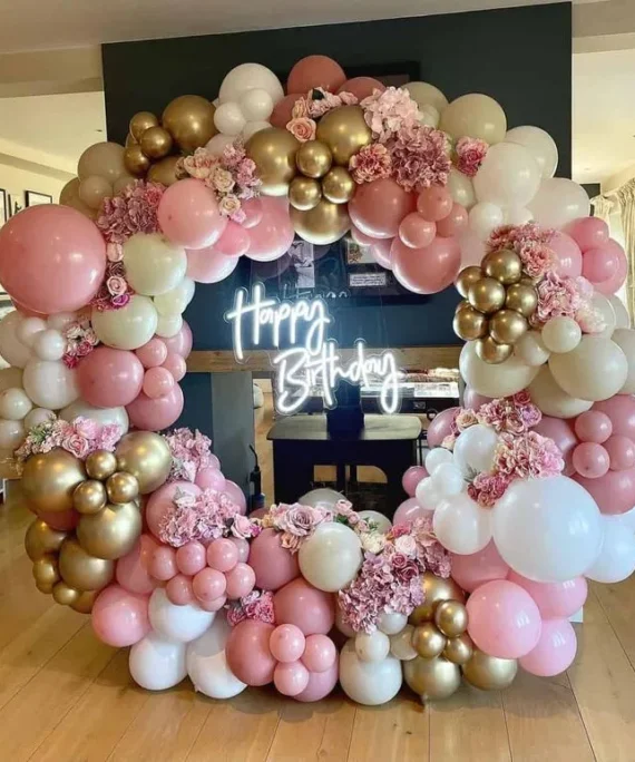 Round arch birthday balloon decoration with pink, gold, white cream balloons, artificial pink flowers, and Happy Birthday wall sign in Dubai, UAE by Event Experts.