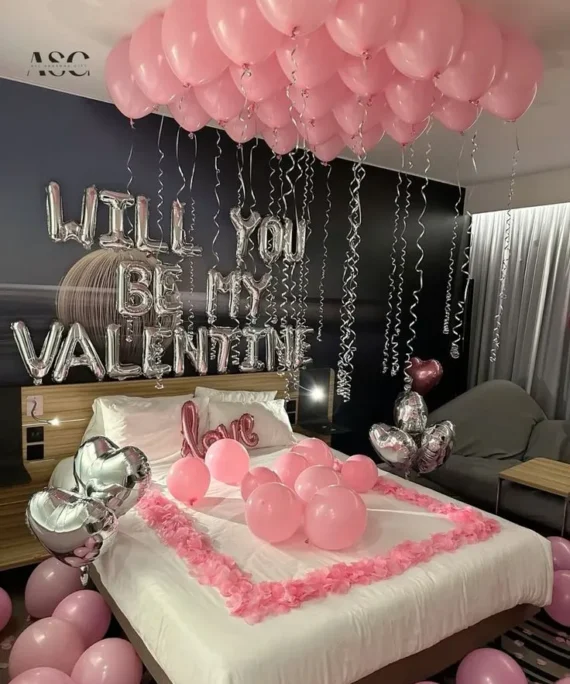 Valentine’s Day balloon decoration with pink helium balloons, 6 silver heart foil helium balloons, love foil balloon, Valentine foil silver, floor balloons, and rose petals on bed in Dubai, UAE by Event Experts.
