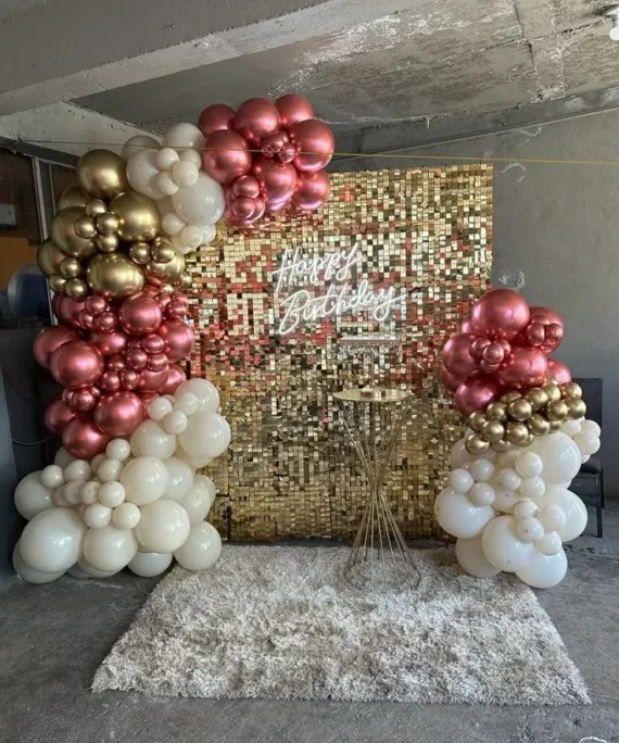 Golden shimmer half arch birthday balloon decoration with rose gold, cream, golden, and white balloons, square cake table, and Happy Birthday wall sign in Dubai, UAE by Event Experts.