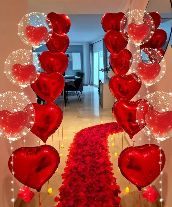 Valentine’s Day balloon decoration with 12 red helium balloons, 6 red heart foil balloons, bobo helium heart balloons, lights, candles, and red rose petals on the floor in Dubai, UAE by Event Experts.