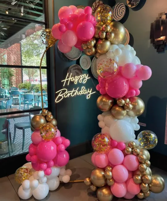 Half arch birthday balloon decoration with golden, white, light pink, dark pink and transparent balloons with Happy Birthday wall sign in Dubai, UAE by Event Experts.