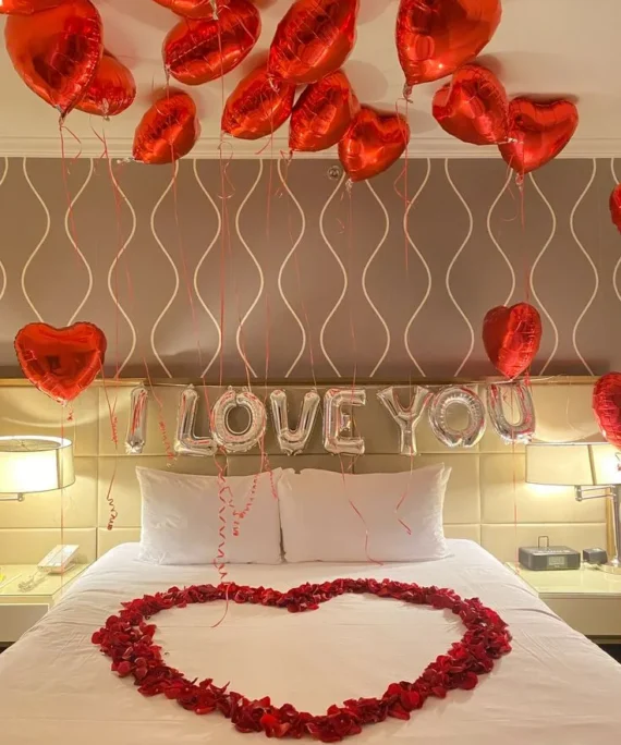 Valentine’s Day balloon decoration with 15 red heart helium foil balloons on the wall, “I Love You” silver foil balloon, and rose petals on the bed in Dubai, UAE by Event Experts.
