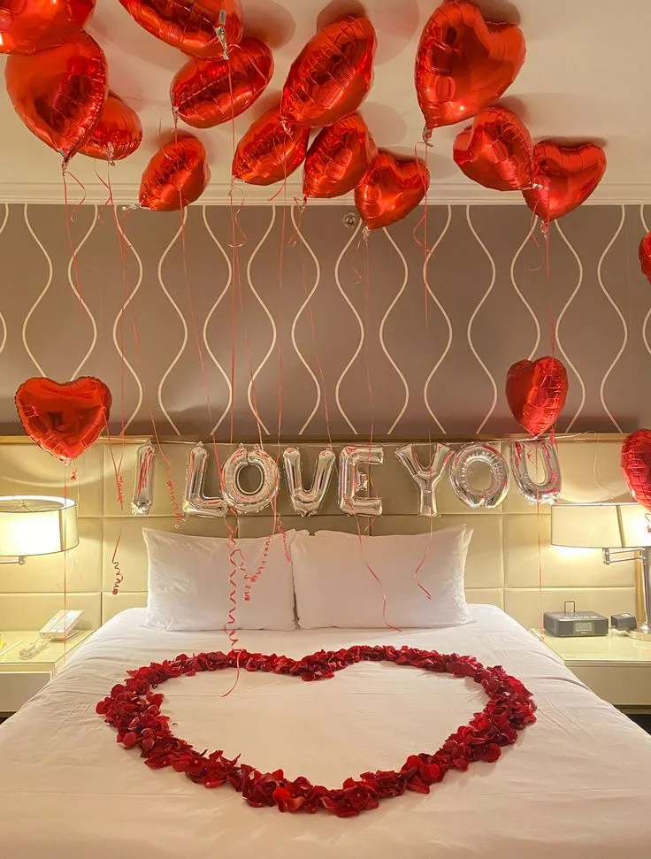 Valentine’s Day balloon decoration with 15 red heart helium foil balloons on the wall, “I Love You” silver foil balloon, and rose petals on the bed in Dubai, UAE by Event Experts.