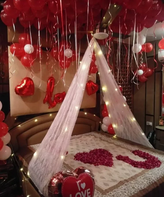 Valentine’s Day balloon decoration with 50 red balloons on the wall, 2 red heart foil balloons, 5 flower balloons, red Love foil, big Love heart foil, red rose petals on the bed, and white net cloth with lights in Dubai, UAE by Event Experts.