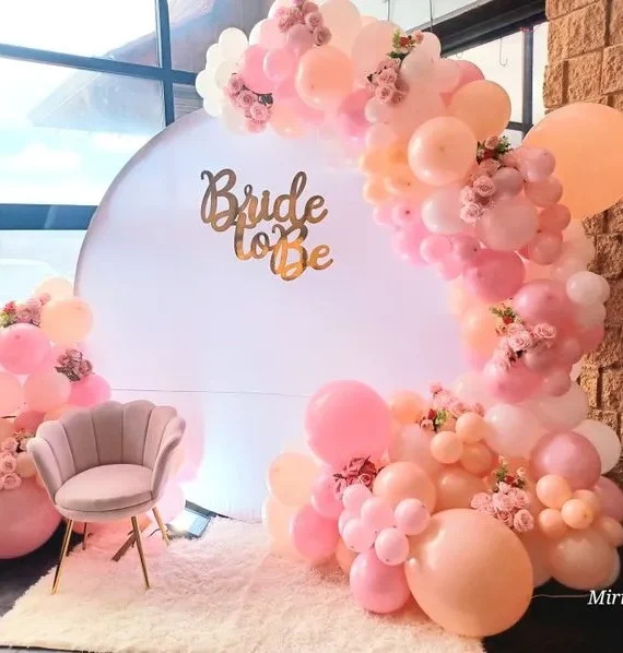 Bridal shower balloon half arch setup with light pink, white and peach cream balloons, artificial roses, bride to be banner and white round backdrop by Event Experts UAE