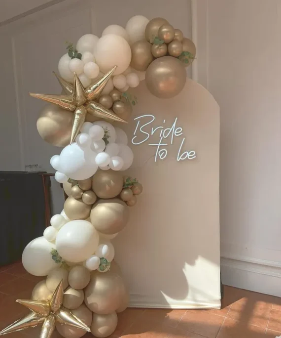 Bridal shower half arch balloon setup with white, sand white and metallic gold balloons, gold foil stars and bride to be banner by Event Experts UAE