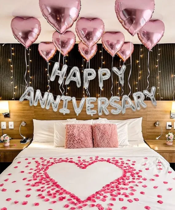 Anniversary room setup with helium pink heart balloons, 50 pink floor balloons, silver happy anniversary banner and rose petals on bed by Event Experts UAE