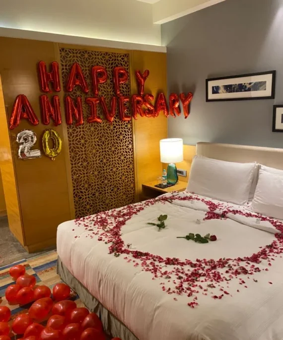 Anniversary room decoration with 50 red balloons on wall, 50 red balloons on floor, red happy anniversary banner and rose petals on bed by Event Experts UAE