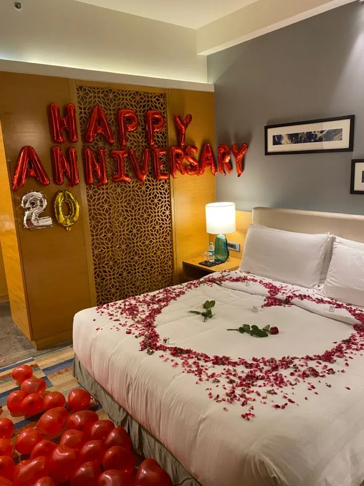 Anniversary room decoration with 50 red balloons on wall, 50 red balloons on floor, red happy anniversary banner and rose petals on bed by Event Experts UAE