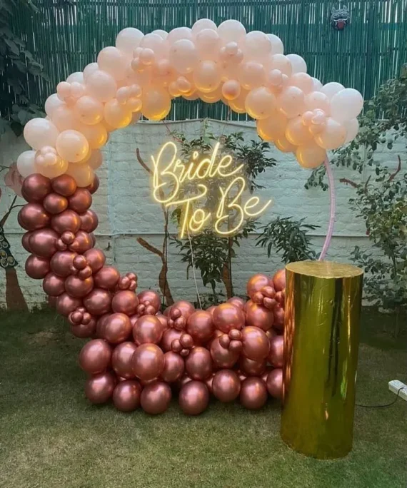 Bridal shower half arch balloon setup with cream peach, sand white and rose gold balloons, white round cake table and bride to be banner by Event Experts UAE