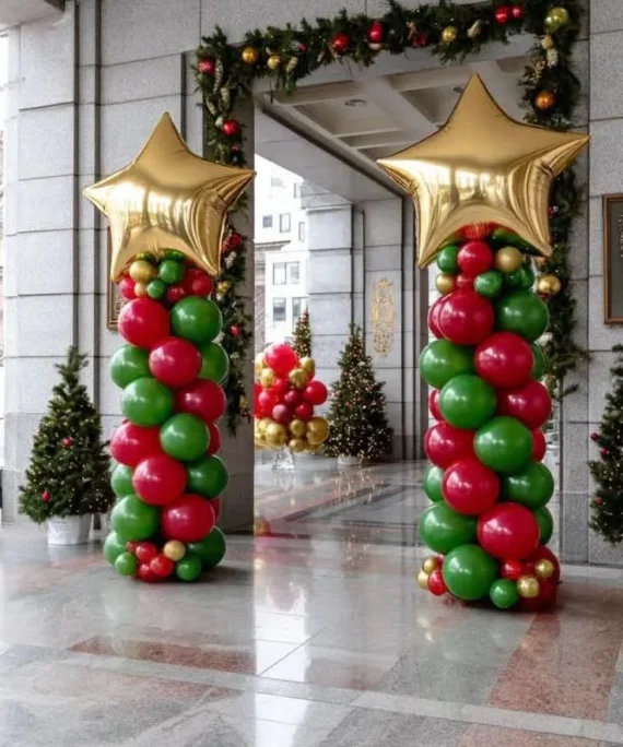 Christmas garland arch and balloon pillar decoration with red, green, gold balloons, golden foil star balloons, Christmas ornaments, festive garlands, and a large Christmas tree.
