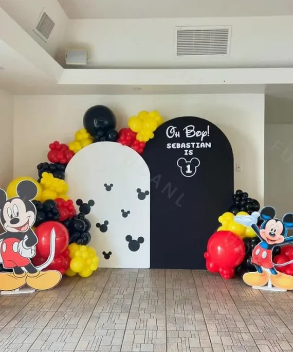 Mickey Mouse theme balloon birthday backdrop decoration with red, yellow, and black balloons, white and black backdrops, and two Mickey Mouse character cutouts.