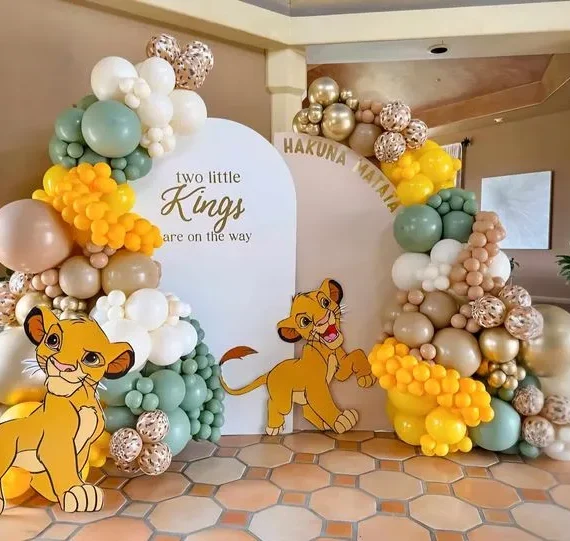 Hakuna Matata Simba theme balloon setup with dusty yellow, beige, gold, white, rose gold, and silver balloons, two half arch backdrops, lion cutouts, and rose gold foil balloons.