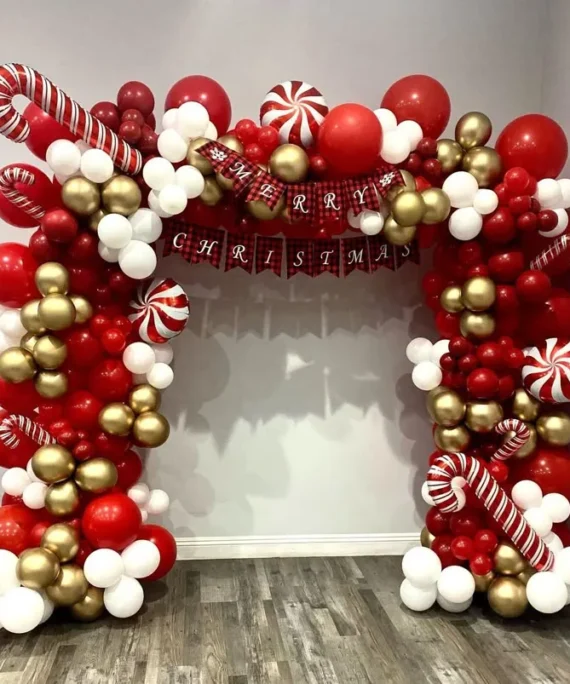 Christmas full arch balloon setup with red, white, and gold balloons, Merry Christmas banner, candy cane decorations, and candy foil balloons.