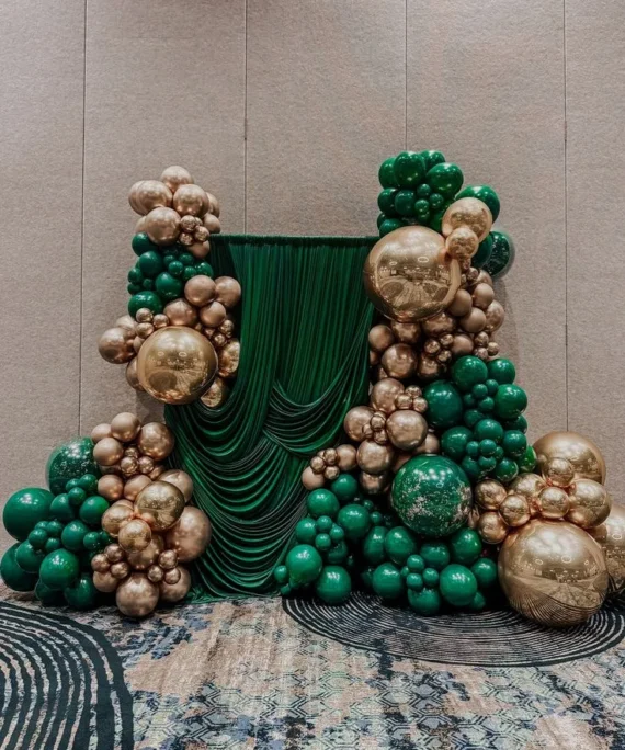 Mehndi balloon curtain backdrop decoration setup with dark green and rose gold balloons, oversized balloons, and elegant backdrop curtains for a Mehndi ceremony.