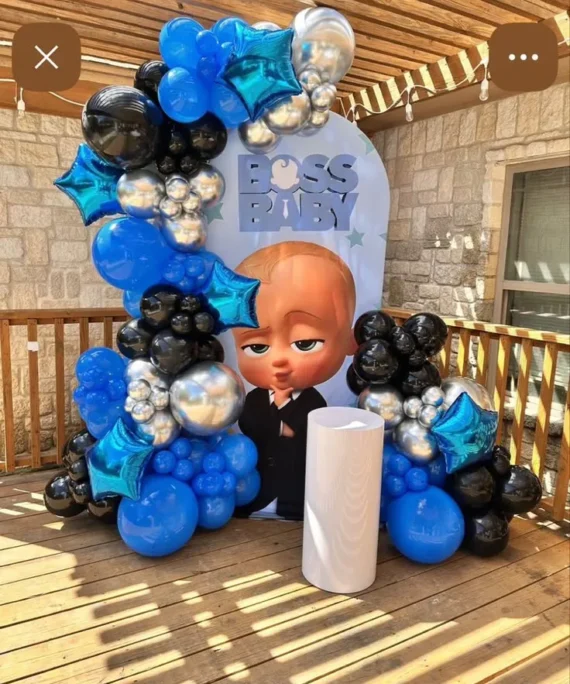 Baby Boss theme balloon arch backdrop setup with dark blue, silver, black balloons, blue foil star balloons, and white cake table decoration.