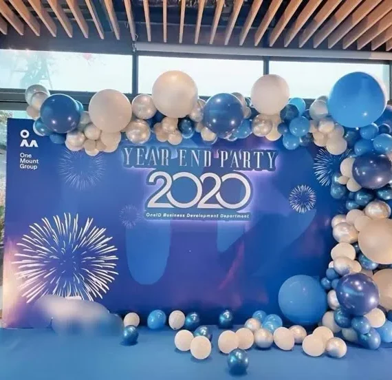 Year end party corporate event half arch balloon decoration setup with ocean blue and white balloons, printed backdrop, large balloons, floor balloons, wall hanging balloon bunches, and white round cake tables.