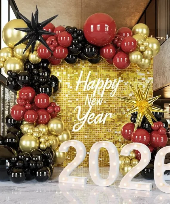 Happy New Year 2027 shimmer panel balloon decoration setup with red, black, and gold balloons, black and gold foil star balloons, Happy New Year foil banner, and golden square cake tables.