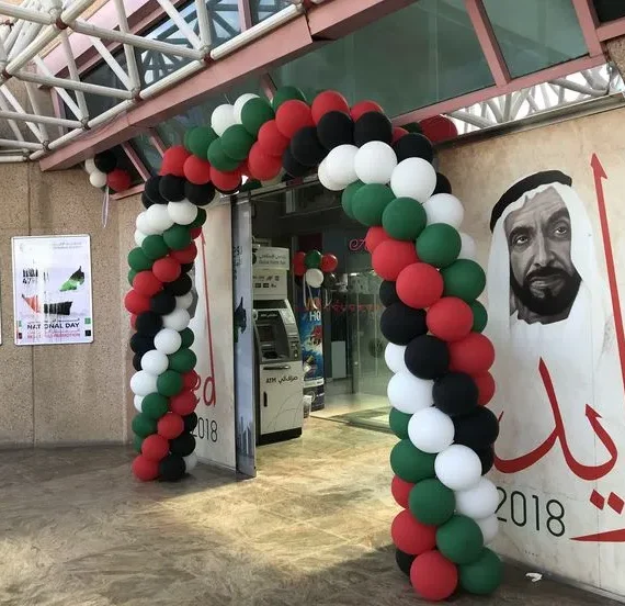 UAE National Day office entrance arch balloon decoration with red, black, green, and white balloons, 15 hanging balloon bunches, and one UAE flag.