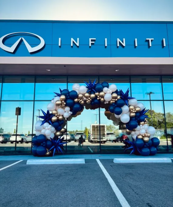 Corporate office entrance balloon arch decoration setup with white, rose gold, dark blue, and off white balloons, star foil balloons, balloon pillars, hanging balloons, and white round cake table.