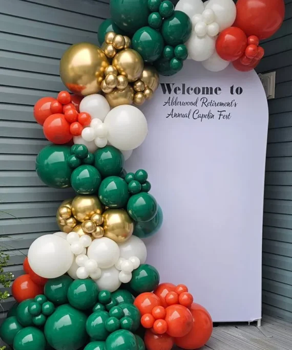 UAE National Day half arch balloon backdrop decoration setup with black, white, red, green, and gold balloons, National Day printed backdrop board, and white round cake table.