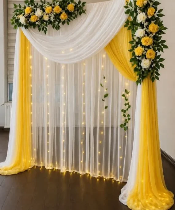 Haldi ceremony net backdrop artificial flower decoration setup with yellow and white flowers, green artificial leaves, LED lights, and Haldi ceremony foil banner.